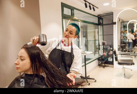 Der kreative weibliche Friseur trocknet die Haare der Kunden mit einem Haartrockner im Schönheitssalon Stockfoto