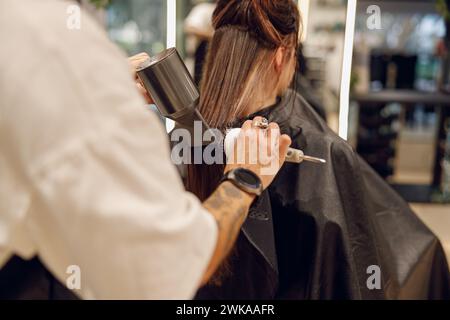 Rückansicht des weiblichen Friseurs trocknet die Haare des Kunden mit einem Haartrockner im Schönheitssalon Stockfoto