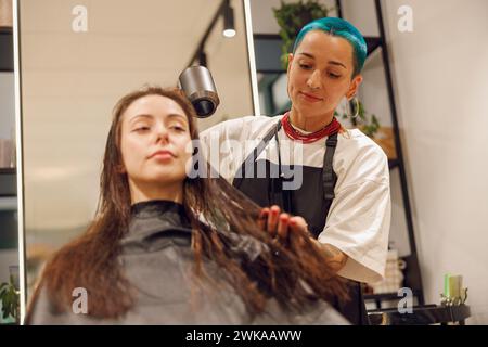 Der kreative weibliche Friseur trocknet die Haare der Kunden mit einem Haartrockner im Schönheitssalon Stockfoto