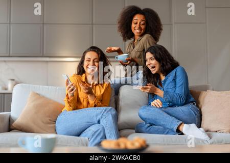 Drei fröhliche, multirassische Freundinnen lachen im Wohnzimmer Stockfoto