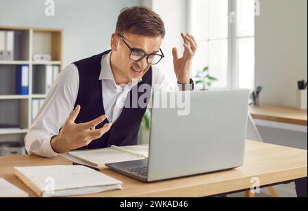 Unzufriedener junger Geschäftsmann, der im Büro sitzt und auf den Bildschirm des Laptops blickt Stockfoto