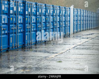 Eine Linie blauer Versandbehälter, die als Lagereinheiten verwendet wurden, die an einem regnerischen Tag fotografiert wurden. Stockfoto