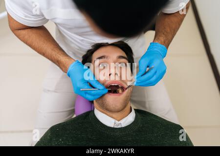 Porträt eines gutaussehenden männlichen Patienten, der im stomatologischen Sitz mit offenem Mund bei nicht erkennbarer Zahnärztin liegt, mit Zahnarzt Stockfoto