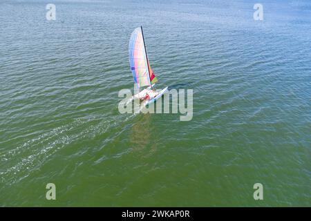 Drohnenansicht eines Katamarans, das im türkisfarbenen Wasser des El Portil Beach mit einem mehrfarbigen Segel in Punta Umbria Municipali segelt Stockfoto