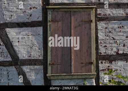 Details eines Fachwerkhauses, das renovierungsbedürftig ist, die Fensterläden sind geschlossen, die Armaturen sind verrostet, weiße Steinwände, die Farbe blättert ab Stockfoto