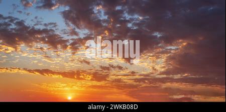 Die Sonne geht oder untergeht am Horizont, leuchtend orange Farben, lockige Wolken. Stockfoto