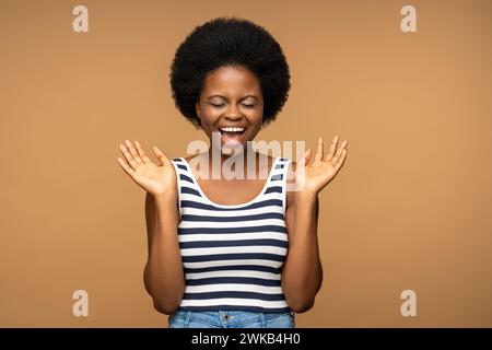 Emotional überglücklich, schwarze Frau, breit lächelt mit geschlossenen Augen und Händen hoch Stockfoto