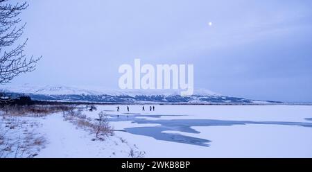 Die Leute laufen auf dem Eis in Laugarvatn, Island, wenn ein Vollmond auftaucht Stockfoto