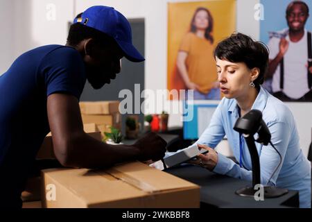 Kaukasischer Manager unterschreibt Logistikdateien und bespricht Lieferdetails mit dem Kurier im Bekleidungsgeschäft. afroamerikanischer Lieferer bereitet sich auf den Versand von Online-Bestellungen in modernen Boutiquen vor Stockfoto