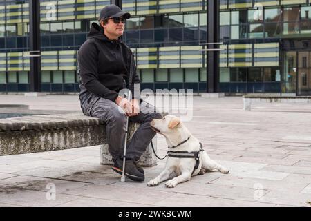 Der blinde Mann und sein Blindenhund sitzen auf der Straße. Sehbehinderte Menschen und Assistenzhunde Konzept. Stockfoto