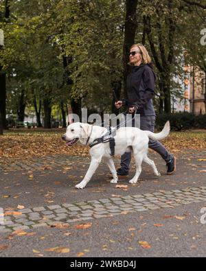 Eine blinde Frau in Begleitung ihres treuen Begleithundes, die sicher und entspannt durch einen Stadtpark läuft. Stockfoto