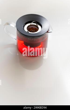 Eine Teekanne aus Glas mit einem Fruchtaufguss, Infuser Pitcher mit einem Erdbeeraufguss, roter Tee, Apfel oder Beerenaufguss auf einem weißen Tisch, vertikal Stockfoto