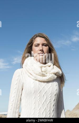 Frau in einem weißen Pullover und Schal, stehend vor einem Hintergrund aus Himmel und Felsen Stockfoto