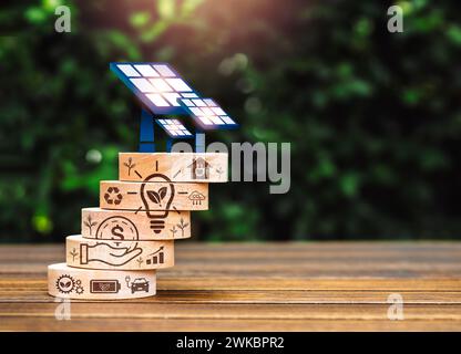 Nachhaltigkeit Öko, Erdpflege, Energieeinsparung und Energiekonzept. Solarpaneele werden auf Holzwürfelstapel mit Symbolen für das Ökosystem auf Holz installiert Stockfoto