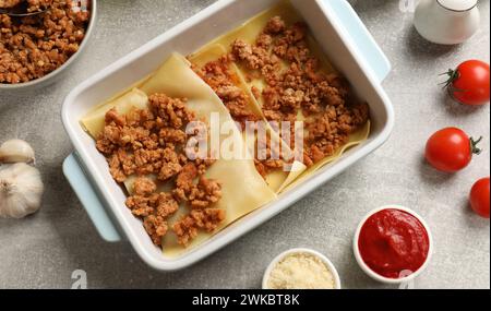 Lasagne kochen. Pasta-Blätter, Hackfleisch in Backblech und Produkte auf einem hellen, strukturierten Tisch, flach liegend Stockfoto
