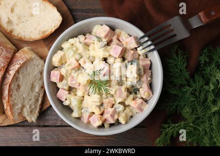 Leckerer Olivier-Salat mit gekochter Wurst in Schüssel auf Holztisch serviert, flach gelegt Stockfoto