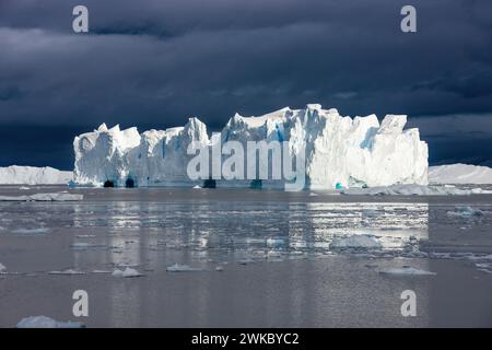 Großer Eisberg mit Eishöhlen, die von einem Schelfeis abgetrennt wurden, unter einem stürmischen Himmel, Antarktische Halbinsel, Antarktis Stockfoto