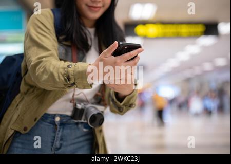 Ein Nahbild einer asiatischen Reisenden oder Passagierin überprüft ihre Fluginformationen auf ihrem Smartphone, bevor sie am Schalter im airpo einchecken Stockfoto