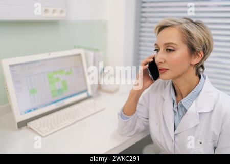 Großaufnahme einer blonden Ärztin mittleren Alters, die am Schreibtisch mit Laptop sitzt, Empfehlung erklären, Untersuchungsergebnisse dem Patienten besprechen Stockfoto