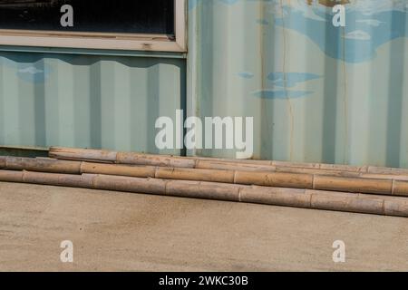 Verwitterte, rissige Bambusstangen auf Betoneinfahrt vor der Aluminiumwand in Südkorea Stockfoto