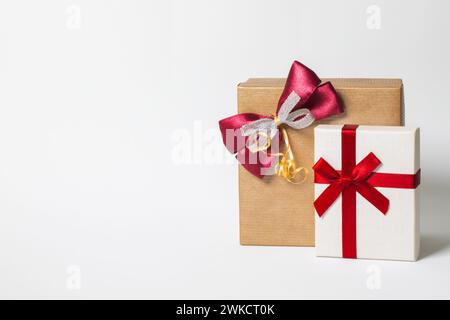 Zwei Geschenkboxen, die in Papier gewickelt und mit Schleife und Schleifen auf weißem Hintergrund gebunden sind. Kopierraum.Vorderansicht. Rote, weiße und braune Farben Stockfoto