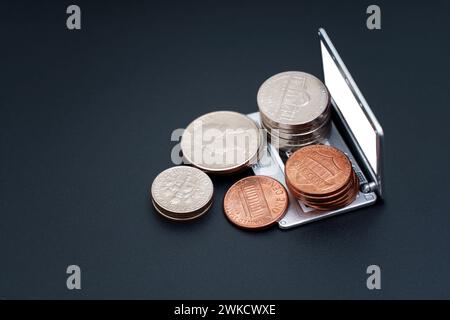Geld online verdienen: Riesige Stapel von Münzen, die elegant auf einem offenen Miniatur-Laptop angeordnet sind, isoliert auf Schwarz. Stockfoto
