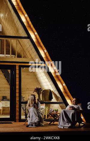 Ruhiges Gespräch zwischen Mann und Frau auf der Terrasse der A-Frame-Kabine am Abend Stockfoto