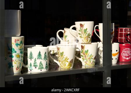 Weiße und rote Tassen mit verschiedenen Designs in einem kleinen Schaufenster mit schwarzem Hintergrund. Stockfoto