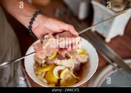 Eine Person bereitet marinierte Kebabs auf Spießen für ein Sommergrillen im Hinterhof vor, die in Nahaufnahmen aufgenommen werden. Stockfoto