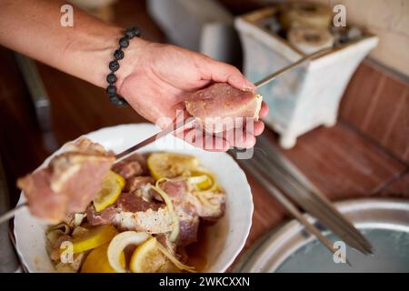 Eine Person bereitet marinierte Kebabs auf Spießen für ein Sommergrillen im Hinterhof vor, die in Nahaufnahmen aufgenommen werden. Stockfoto