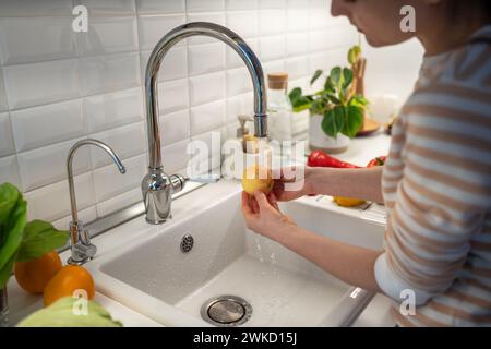 Frauenhände waschen den Apfel in Leitungswasser, um ihn von Wachsparaffin zu reinigen und vor raschem Zerfall zu schützen Stockfoto