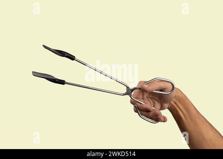 Männliche Hand, die Küchenzange isoliert auf hellgrünem Hintergrund hält Stockfoto
