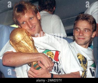 ABGELEGT - 09. Juli 1990, Hessen, Frankfurt/Main: Andreas Brehme (l), ehemaliger deutscher Fußballnationalspieler, hält die WM-Trophäe in den Armen, während sein Teamkollege Thomas Häßler mit einem Lächeln zusieht. Fußball-Weltmeister Andreas Brehme ist im Alter von 63 Jahren gestorben, bestätigt seine Familie gegenüber der Deutschen Presseagentur. (Zu dpa: 'Fußball-Weltmeister Andreas Brehme tot') Foto: Frank Kleefeldt/dpa Stockfoto