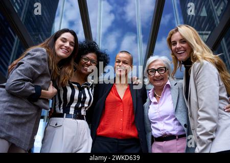 Geschäftsfrauen mit niedrigem Winkel, die sich außerhalb des Büros umarmen, glücklich aussehend, lachend vor der Kamera. Stockfoto