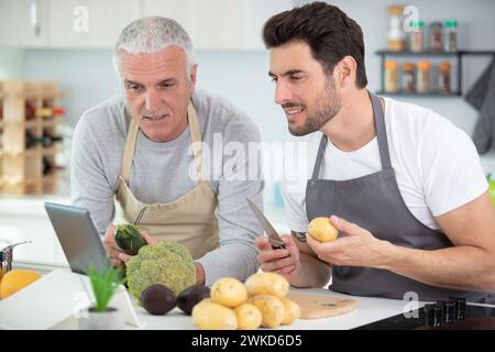 Männer bereiten eine Mahlzeit zu, während sie die Anweisungen auf einer Tablette befolgen Stockfoto