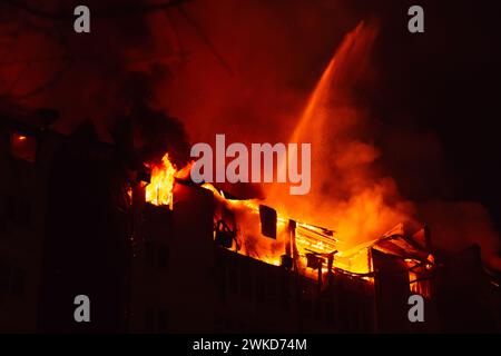 Brennendes Haus ist nachts in Flammen verwickelt. Feuerwehrleute löschen mit Wasser. Feuer im Wohngebäude. Stockfoto