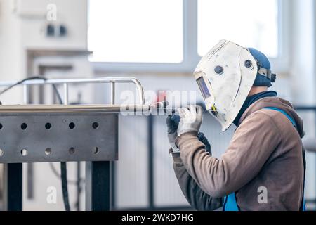 Ein Mann in Arbeitskleidung und Schutzhelm schweißt Metall mit einem pneumatischen Werkzeug Stockfoto