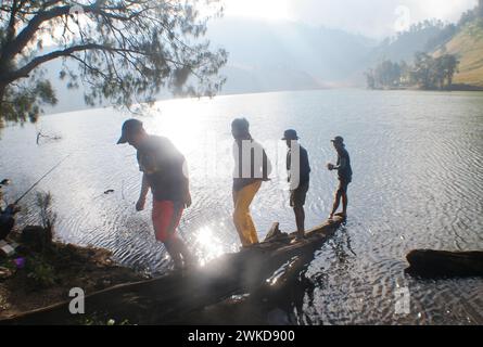Gruppe junger Männer, die auf umgestürzten Baumstämmen am Ufer des Ranu Kumbolo-Sees, Mount Semeru, Indonesien, spazieren. Stockfoto