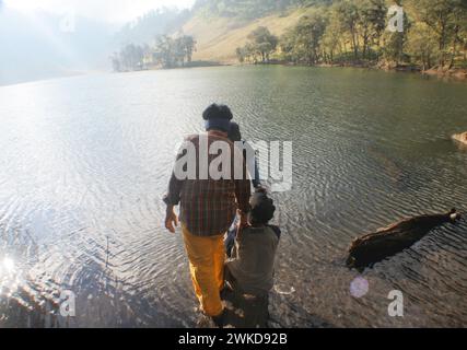 Gruppe junger Männer, die auf umgestürzten Baumstämmen am Ufer des Ranu Kumbolo-Sees, Mount Semeru, Indonesien, spazieren. Stockfoto