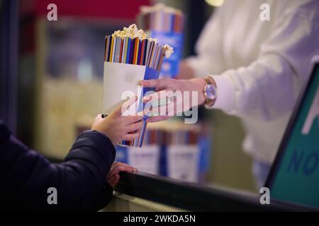 Ein Verkäufer steht vor dem Kino und hält frisches Popcorn, um es an Kinobesucher zu verkaufen, bevor sie das Kino betreten Stockfoto