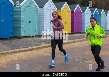 Bournemouth, Dorset, Großbritannien. Februar 2024. Das Wetter in Großbritannien: Ein feuchter Morgen in Bournemouth schreckt Läufer nicht ab, die entlang der Promenade an farbenfrohen Strandhütten vorbeilaufen. Quelle: Carolyn Jenkins/Alamy Live News Stockfoto