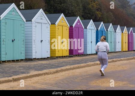 Bournemouth, Dorset, Großbritannien. Februar 2024. Das Wetter in Großbritannien: Ein feuchter Morgen in Bournemouth schreckt Läufer nicht ab, die entlang der Promenade an farbenfrohen Strandhütten vorbeilaufen. Quelle: Carolyn Jenkins/Alamy Live News Stockfoto