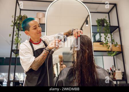 Lächelnde weibliche Friseurin trocknet die Haare des Kunden mit einem Haartrockner im Schönheitssalon Stockfoto