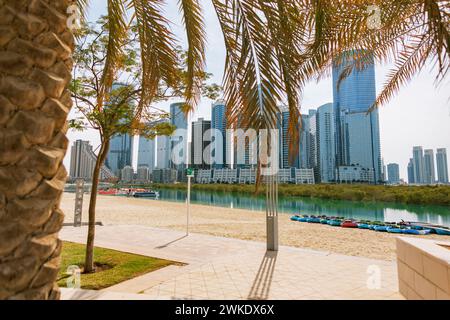 Wunderschöner sonniger Strand mit SUP-Boards, Palmen und moderner Stadtlandschaft in Abu Dhabi, VAE. Sommerruhe. Glasgebäude für Büros und Wohnungen Stockfoto