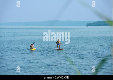 Menschen, die sich sonnen, reiten auf sup Boards auf dem Wasser des großen Flusses, bewaldete Landzunge. Juli 2021. Pereyaslaw-Chmelnyzki, Ukraine Stockfoto