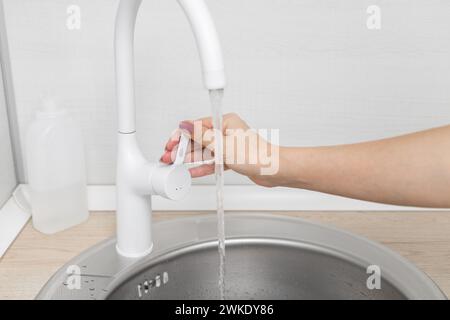 Der Mann öffnet den Wasserhahn in der Küche. Der Mann dreht das Wasser an. Die Hand dreht den Griff eines Küchenarmators. Mit einem Küchenarmatur. Wasser fließt aus der Th Stockfoto