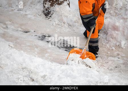 Ein Mann mit einer Schneeschaufel reinigt im Winter Gehwege. Winterzeit. Der Arbeiter entfernt den Schnee vom Weg. Arbeit der Versorgungsbetriebe im Winter Stockfoto