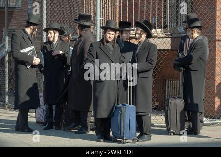 Eine Gruppe orthodoxer jüdischer Männer, einige mit Koffern, wartet auf einen Bus. Sie sind ähnlich gekleidet und wahrscheinlich aus der chassidischen Gruppe Satmar. In Brookly. Stockfoto