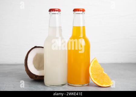 Köstliche Kombucha in Glasflaschen, Kokos und Orange auf grauem Tisch vor weißem Hintergrund Stockfoto