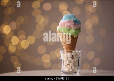 Süße Zuckerwatte in Waffelkegel auf dem Tisch vor verschwommenem Licht, Nahaufnahme. Leerzeichen für Text Stockfoto